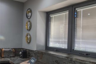 Ventana de cocina con sistema de persianas motorizados y una mano sosteniendo un mando a distancia