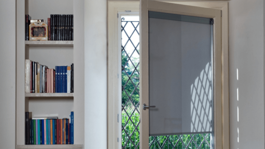 Puerta con cristal y persiana integrada. Al lado una pequeña estantería de pie con libros