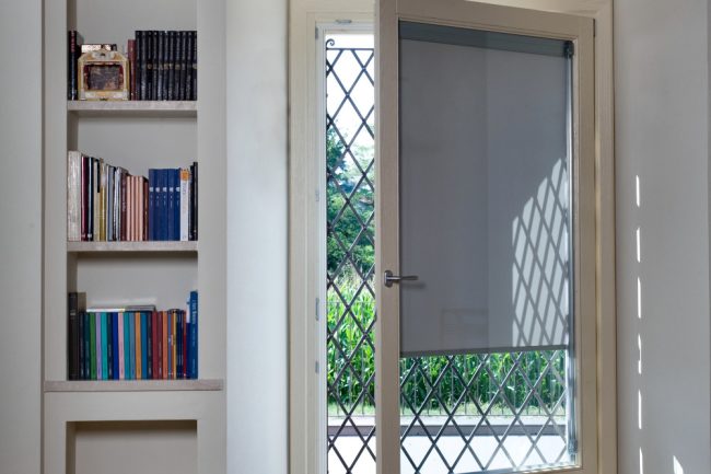 Puerta con cristal y persiana integrada. Al lado una pequeña estantería de pie con libros