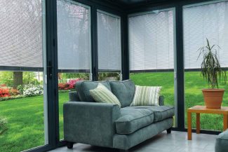 Sofá en sala de estar situado delante de varios ventanales con persianas integradas en cristal