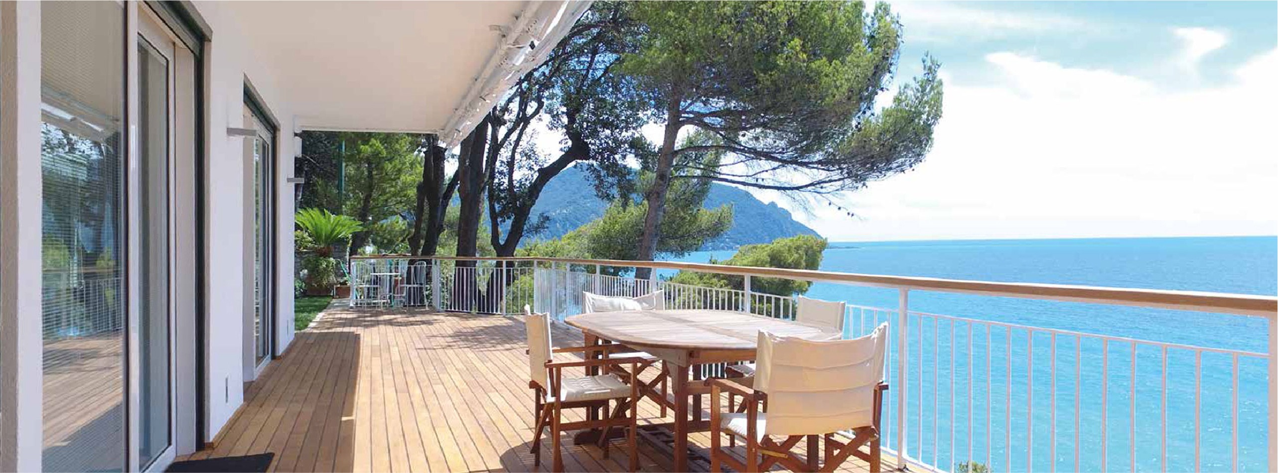 Gran terraza de vivienda situada delante del mar, con una mesa de madera y cuatro sillas