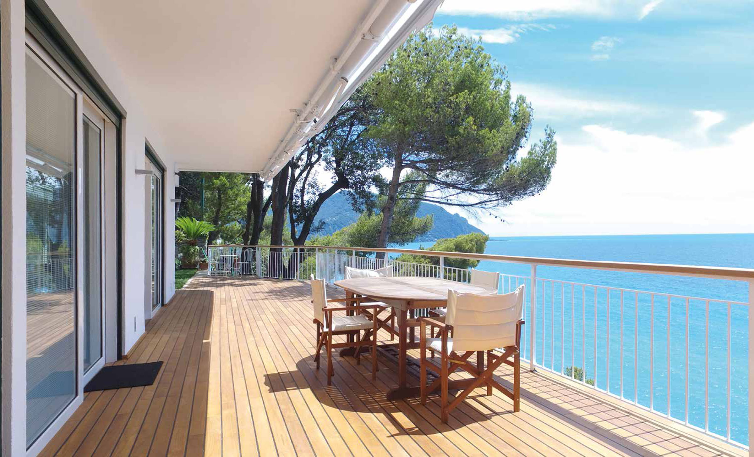 Gran terraza de vivienda situada delante del mar, con una mesa de madera y cuatro sillas